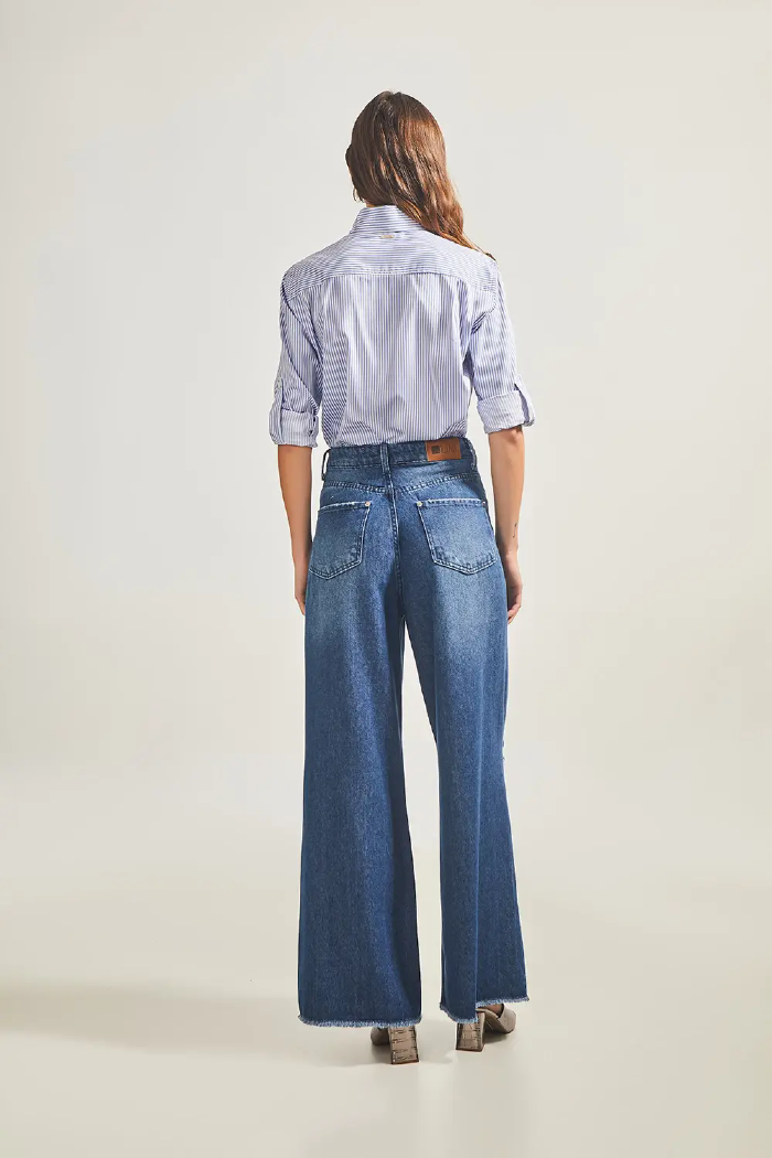 Modelo esta de costas vestindo Calça Jeans Wide Leg Destroyed na cor Jeans Médio e camisa LINI Brazil.