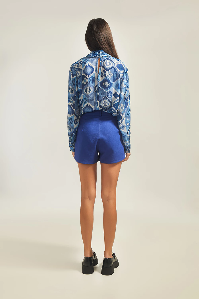 Modelo esta de costas vestindo Shorts Sofia na cor azul escuro e blusa LINI Brazil.